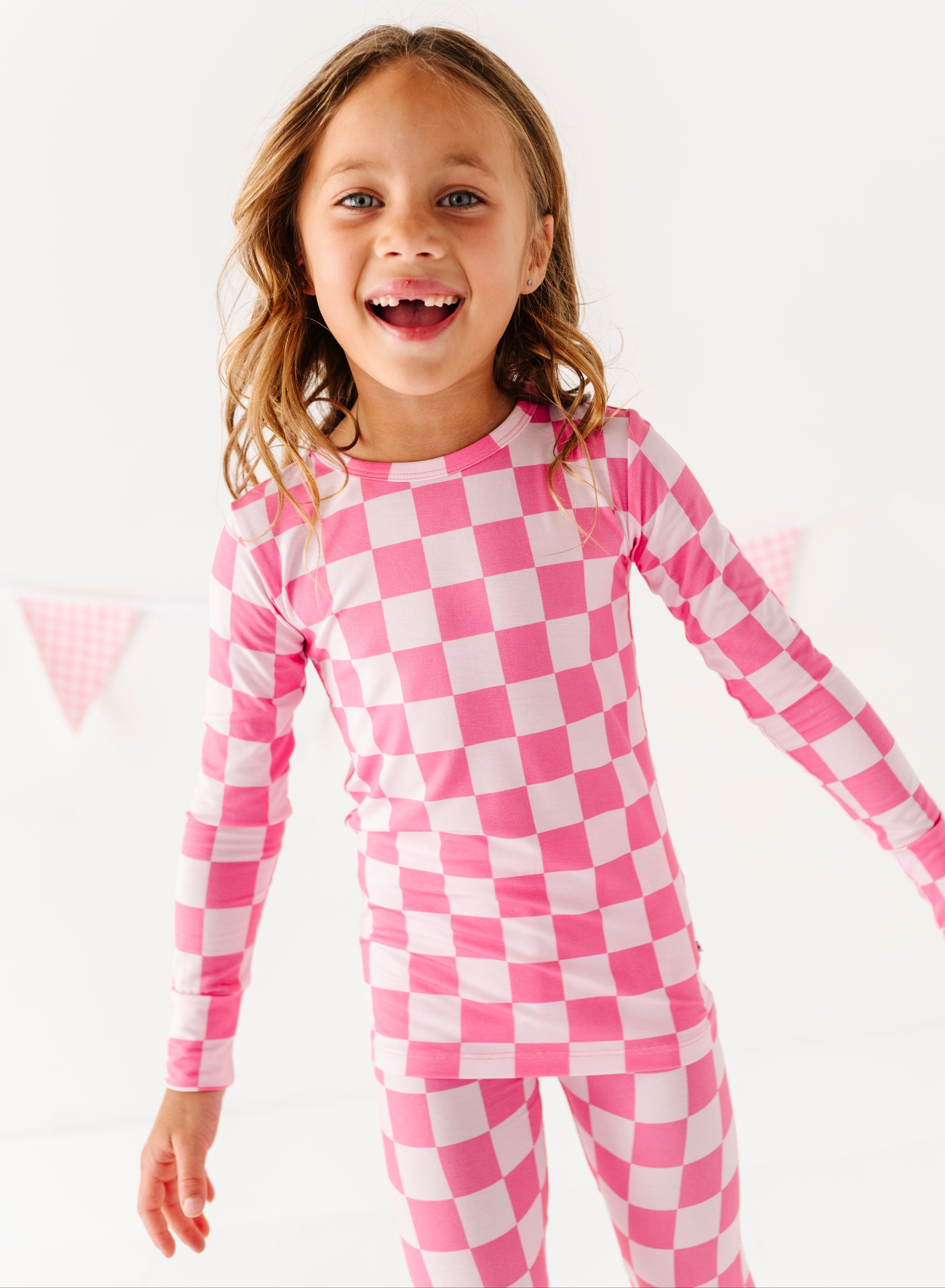 Child wearing pink and white checkered bamboo pajamas on a white background